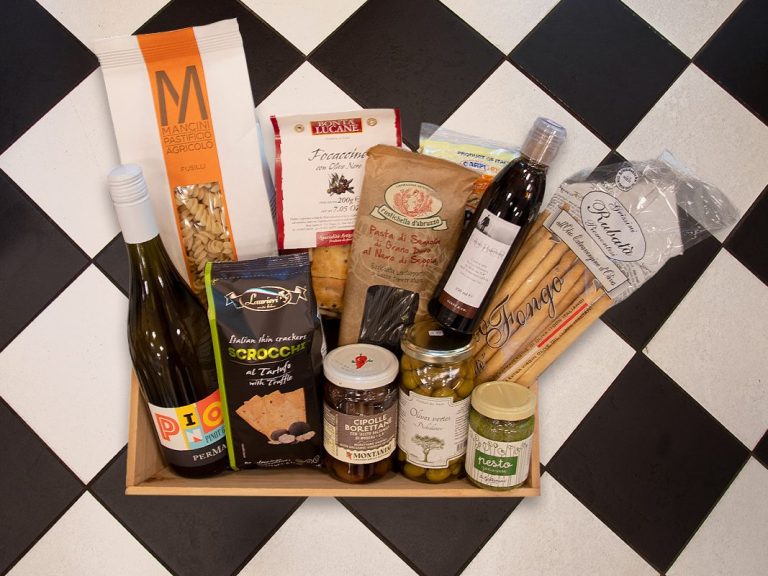 Ein Korb mit Wein, Pasta, Oliven, Keksen und weiteren Lebensmitteln auf einem Schachbrettboden.
