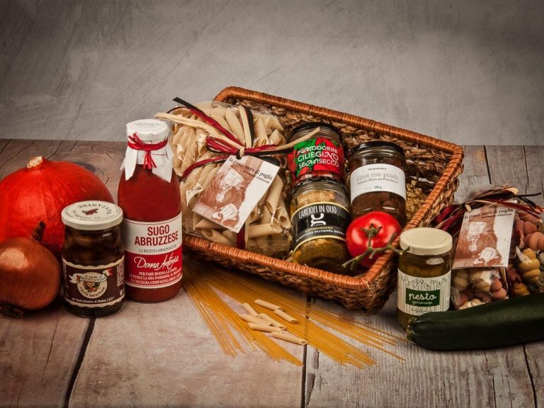 Korb mit Lebensmitteln: Glas, Flasche, Gemüse, Marmelade und Pasta auf Holzuntergrund.